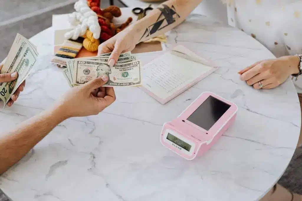 Close-up of hands exchanging US dollars over a marble table with a card reader.